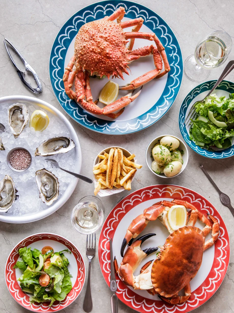 A table filled with fresh seafood in a casual restaurant environment, including spider crab, chancre crab, and oysters