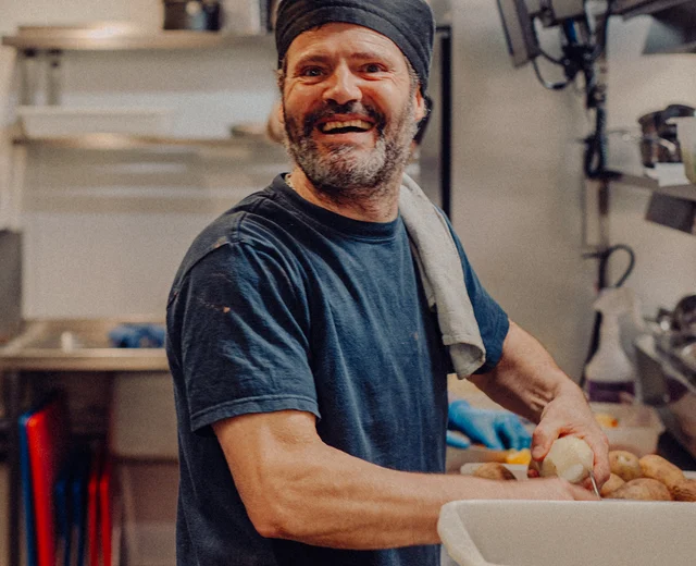A Back of House team member smiles while preparing potatoes
