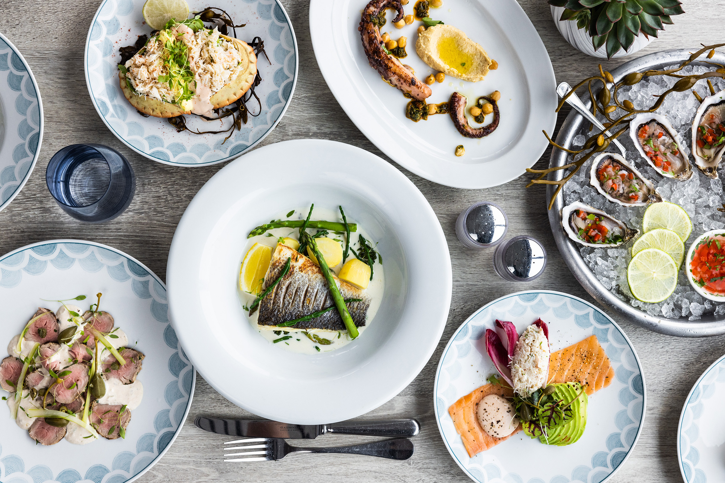 A table filled with seafood dishes, including oysters, octopus, trout, bass, and crab