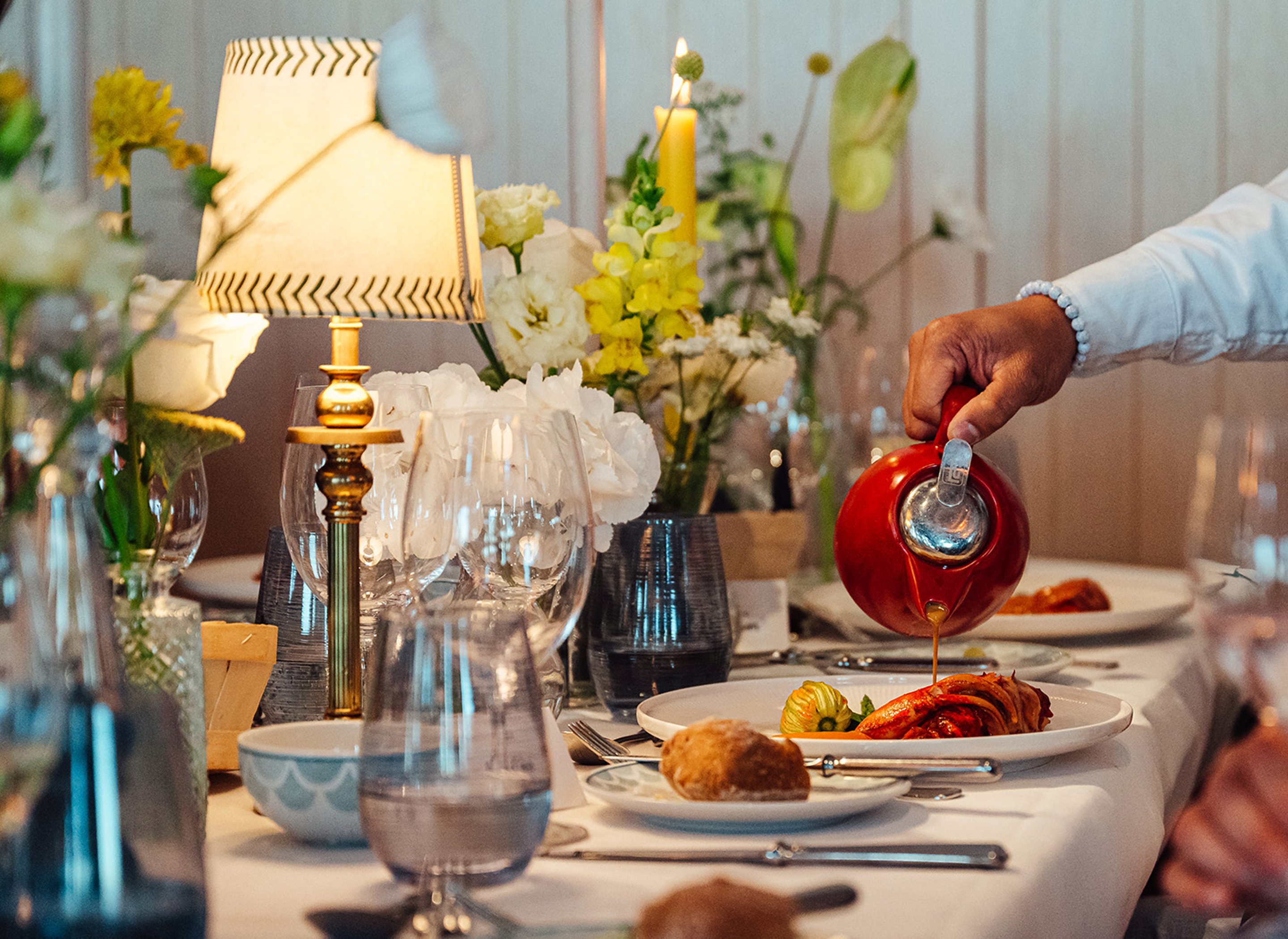 A waiter pours sauce over a main course on a beautifully decorated table