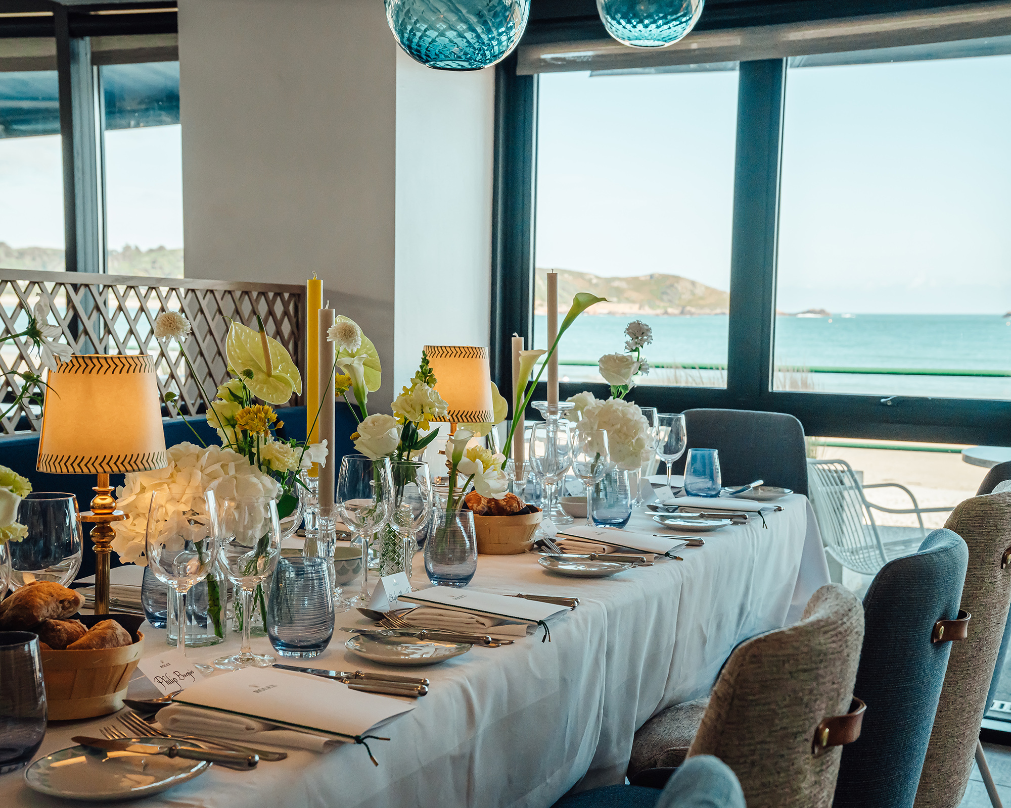 A dining table set up for a private event with floral decorations and views over the Bay
