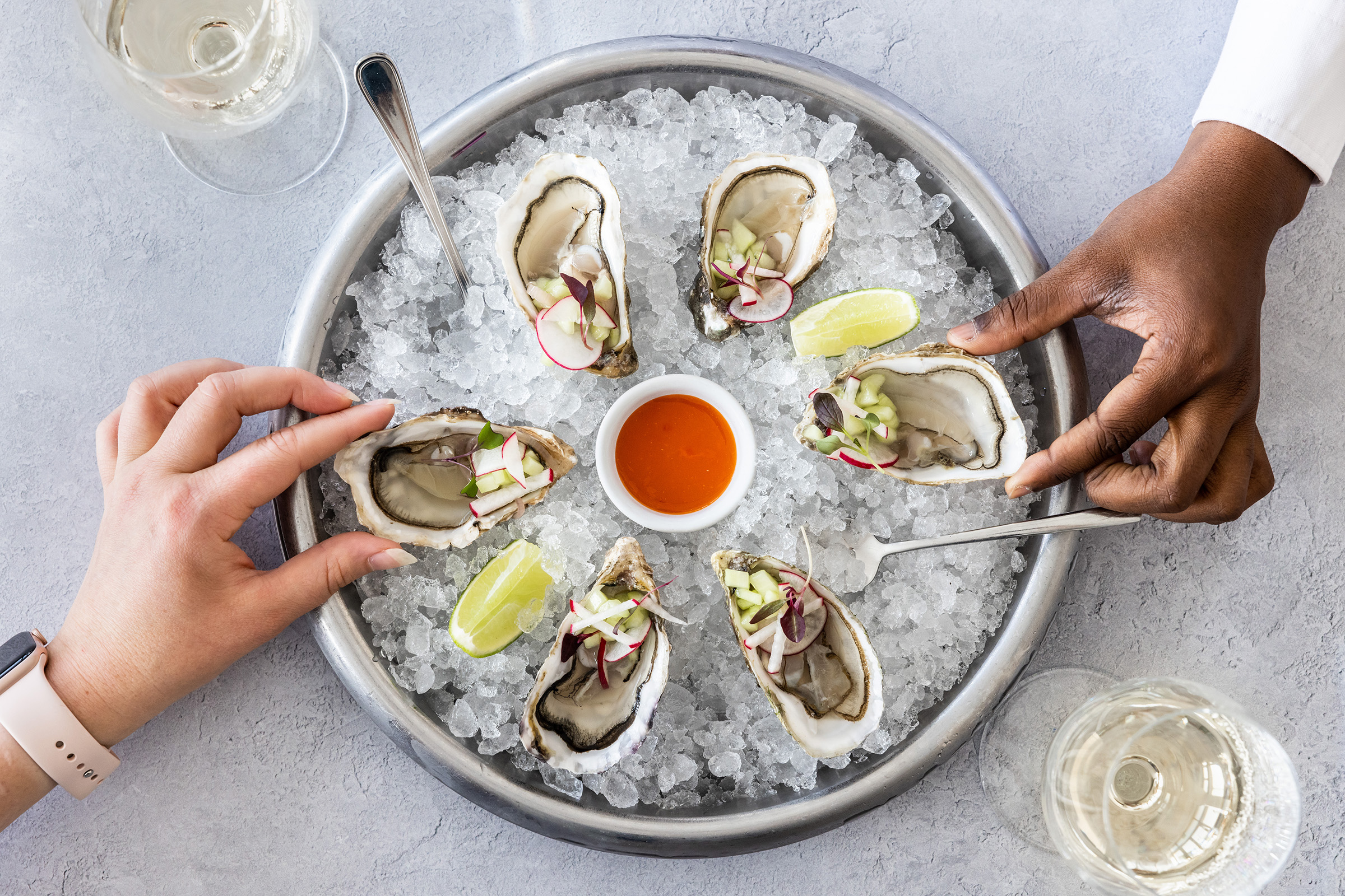 Hands take oysters from a round serving bowl