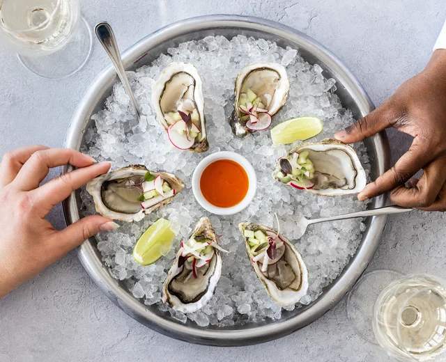 Hands take oysters from a round serving bowl