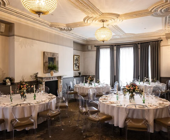 A large private room, set for a wedding reception with round tables, floral decorations and white linen tablecloths