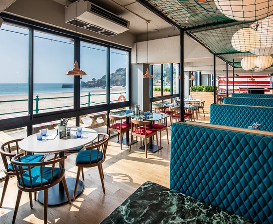 The interior of a nautically-themed seaside restaurant with views over the sand and ocean