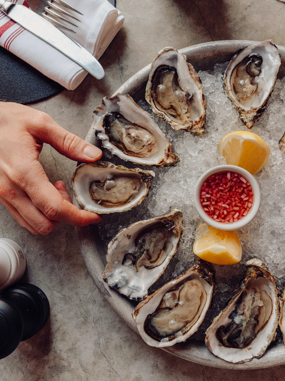 A hand takes a fresh oyster from a plate