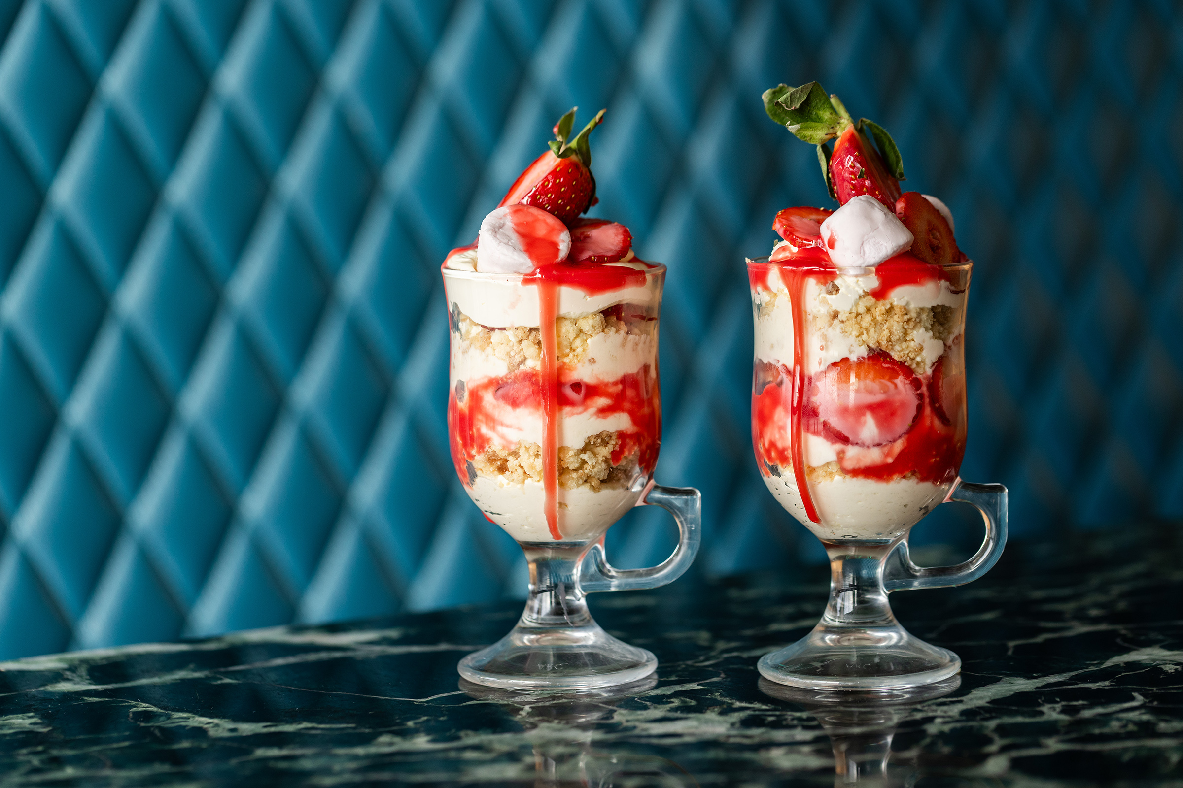 Two tall strawberry trifles in elegant sundae-style glasses