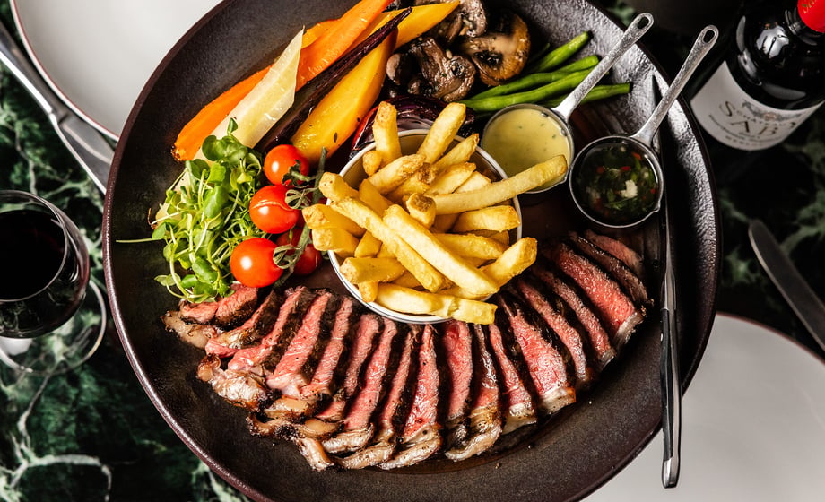 A large plate of Tomahawk steak with chips and vegetables